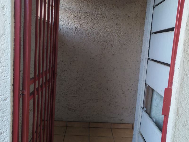 A small utility or service area featuring tiled flooring, a security gate, and a textured wall finish, currently in need of maintenance.