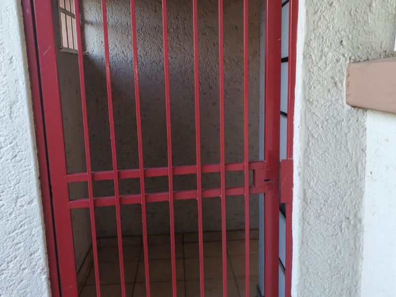 A secure, enclosed utility or storage area featuring tiled flooring, textured walls, and a red metal security gate.