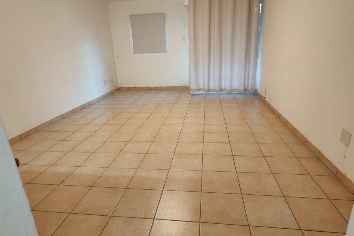 An empty, open-plan living area featuring neutral ceramic floor tiles and a sliding door with a curtain rail, ready for personalization.
