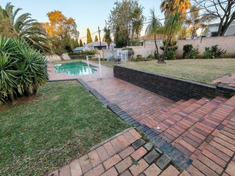 A well-maintained outdoor area featuring a swimming pool, brick-paved patio, tiered retaining walls, and established garden landscaping.