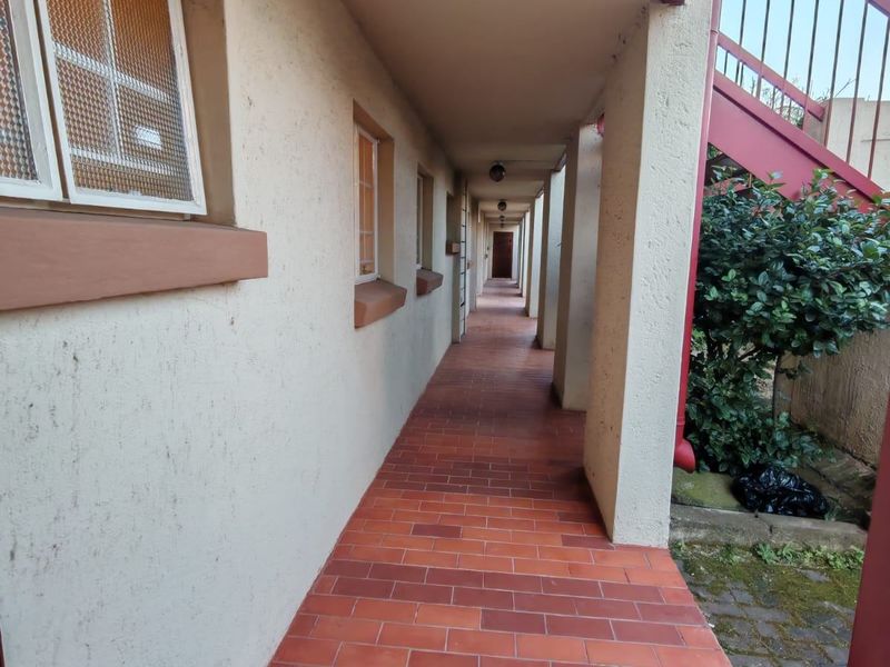An exterior apartment hallway featuring terracotta tiled flooring, overhead lighting, and access to an external staircase.