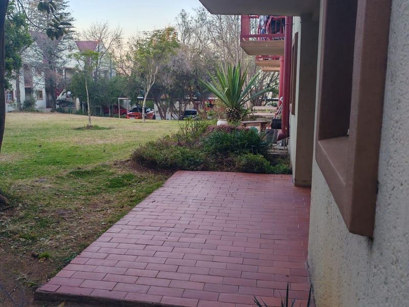 Ground floor brick-paved patio area overlooking a communal garden space with an overhead balcony structure.