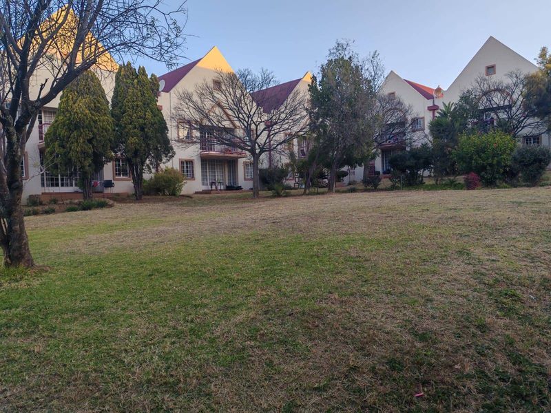 A view of the rear elevation of the apartment complex, featuring pitched roofs, private balconies, and a spacious communal garden area.
