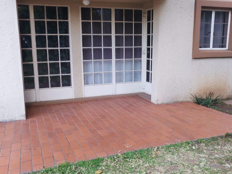 A ground floor patio area featuring terracotta tiling and access via white-framed french doors, situated beneath an upper-level balcony.