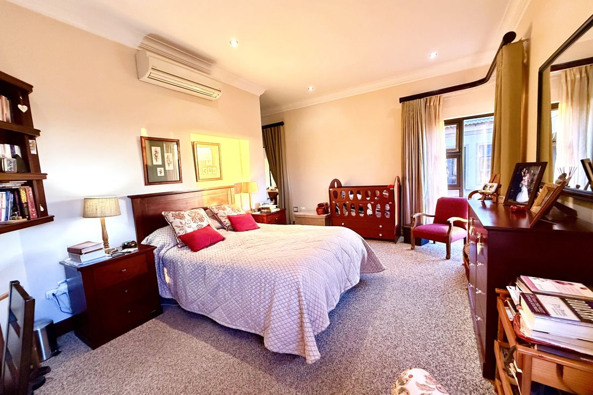 Spacious bedroom featuring wall-mounted air conditioning unit, recessed downlighting, and carpeted flooring with large window providing natural light.