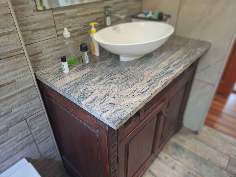 A bathroom vanity featuring a stone countertop, vessel sink, and dark wood cabinetry, complemented by textured stacked stone wall tiles.