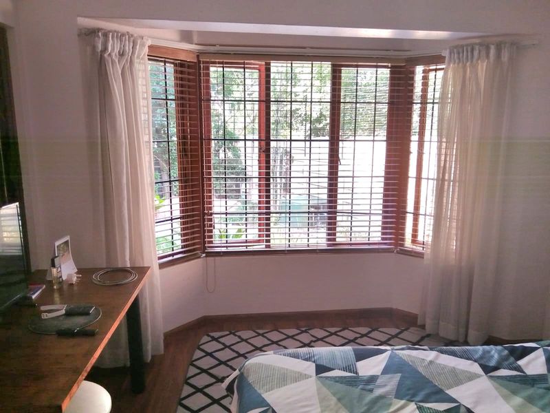 A bedroom featuring a large bay window with timber frames, fitted venetian blinds, and laminate flooring.