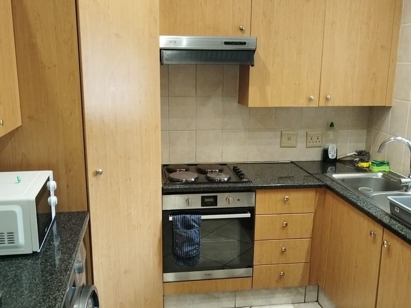 Compact kitchen featuring light wood cabinetry, granite countertops, integrated oven and hob, and tiled flooring.