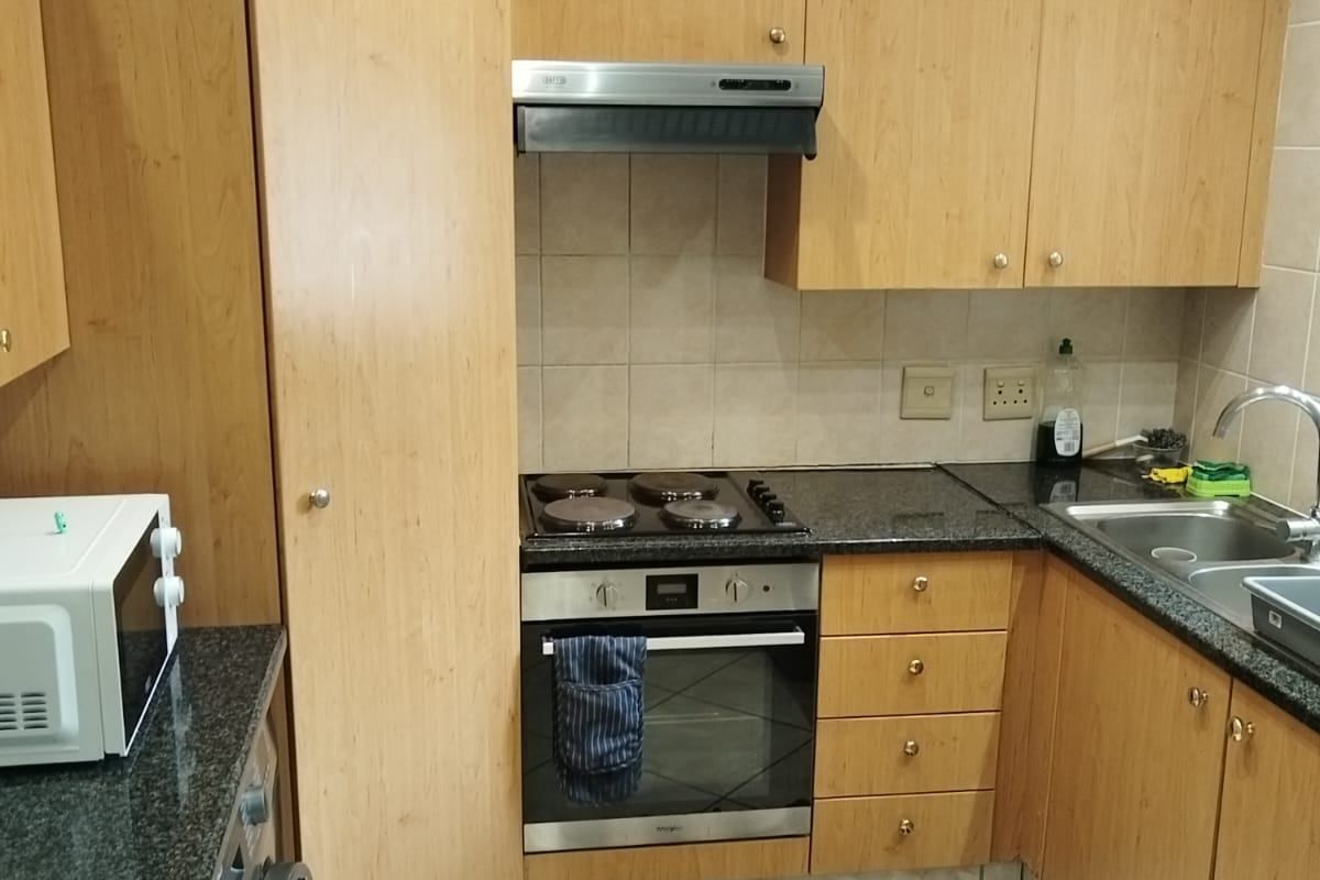 Compact kitchen featuring light wood cabinetry, granite countertops, integrated oven and hob, and tiled flooring.
