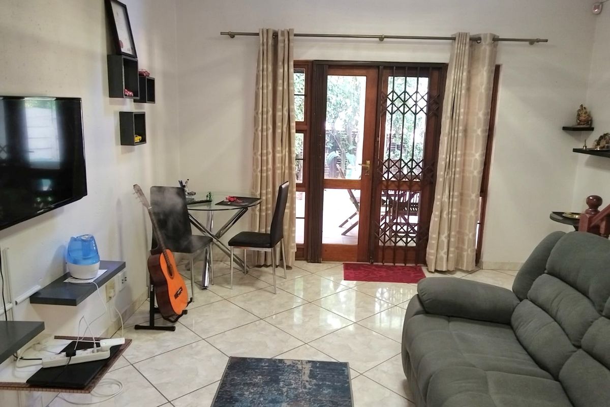 A living room featuring tiled flooring and a timber-framed glass door with a security gate, providing direct access to the outdoor patio area.