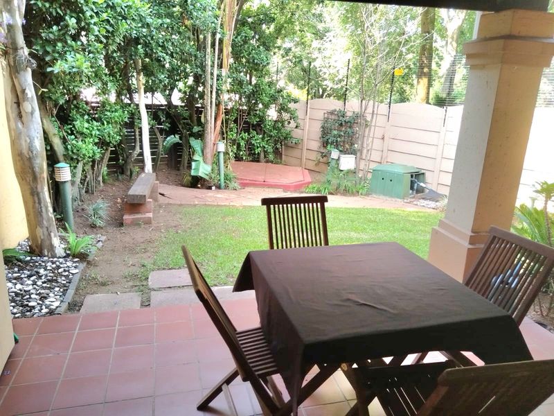A covered patio area overlooking a private garden with a paved path, mature trees, and secure boundary walling with electric fencing.