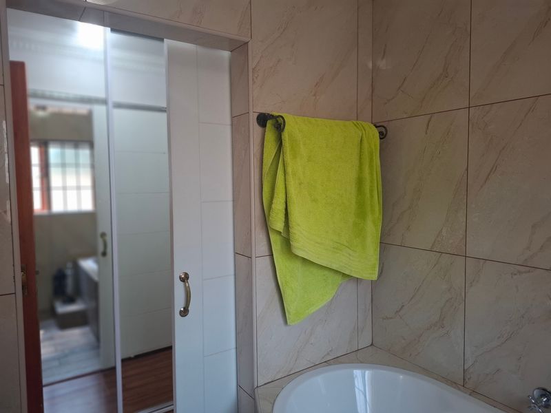 A bathroom featuring neutral wall tiles, a built-in bathtub, and a sliding door leading to an adjacent room.