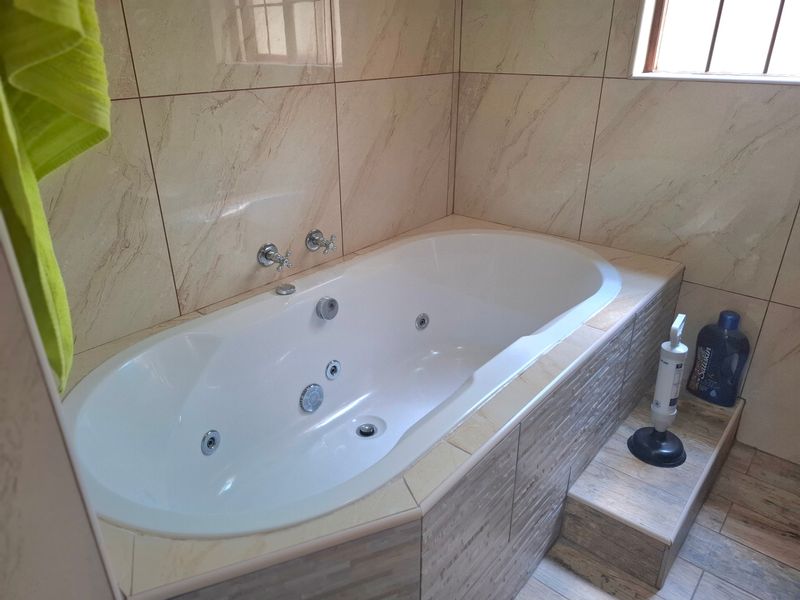 A bathroom featuring a built-in spa bath with chrome fixtures, complemented by neutral-toned wall tiles and a tiled step-up surround.