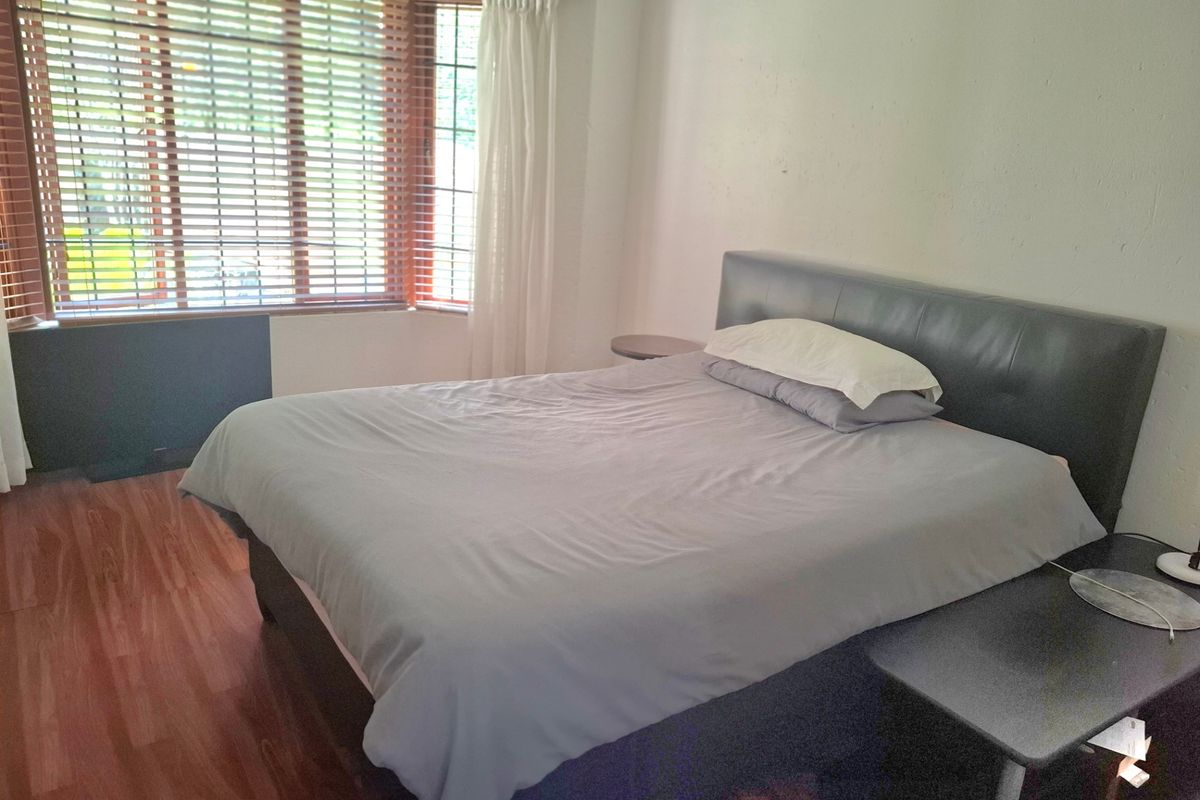 A bedroom featuring laminate flooring and a large bay window with venetian blinds, offering natural light and a functional layout.