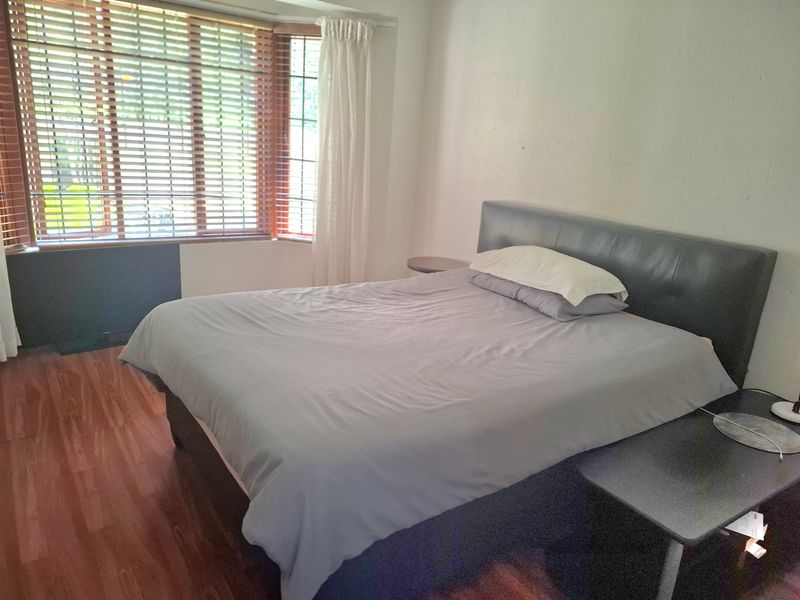 A bedroom featuring laminate flooring and a large bay window with venetian blinds, offering natural light and a functional layout.