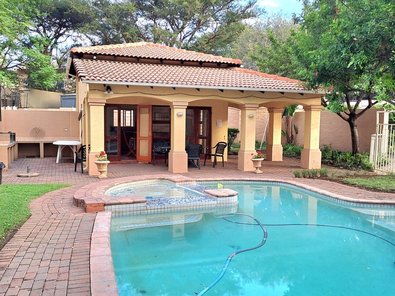 Outdoor entertainment area featuring a swimming pool, brick-paved surround, and a covered patio with a built-in braai.