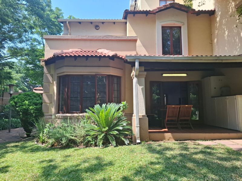 Rear view of the townhouse featuring a covered patio, terracotta roof tiles, and a bay window overlooking a landscaped garden.
