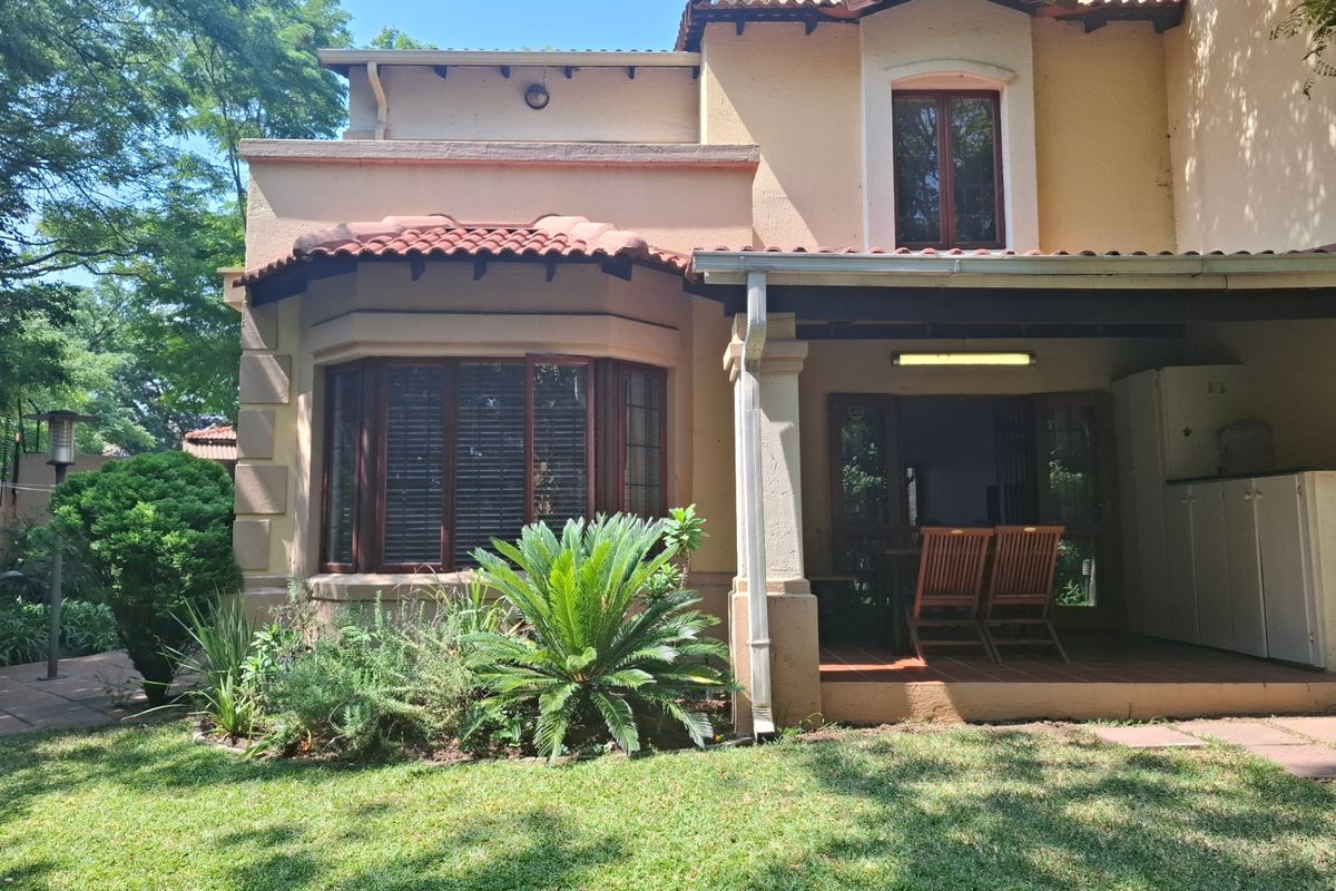 Rear view of the townhouse featuring a covered patio, terracotta roof tiles, and a bay window overlooking a landscaped garden.