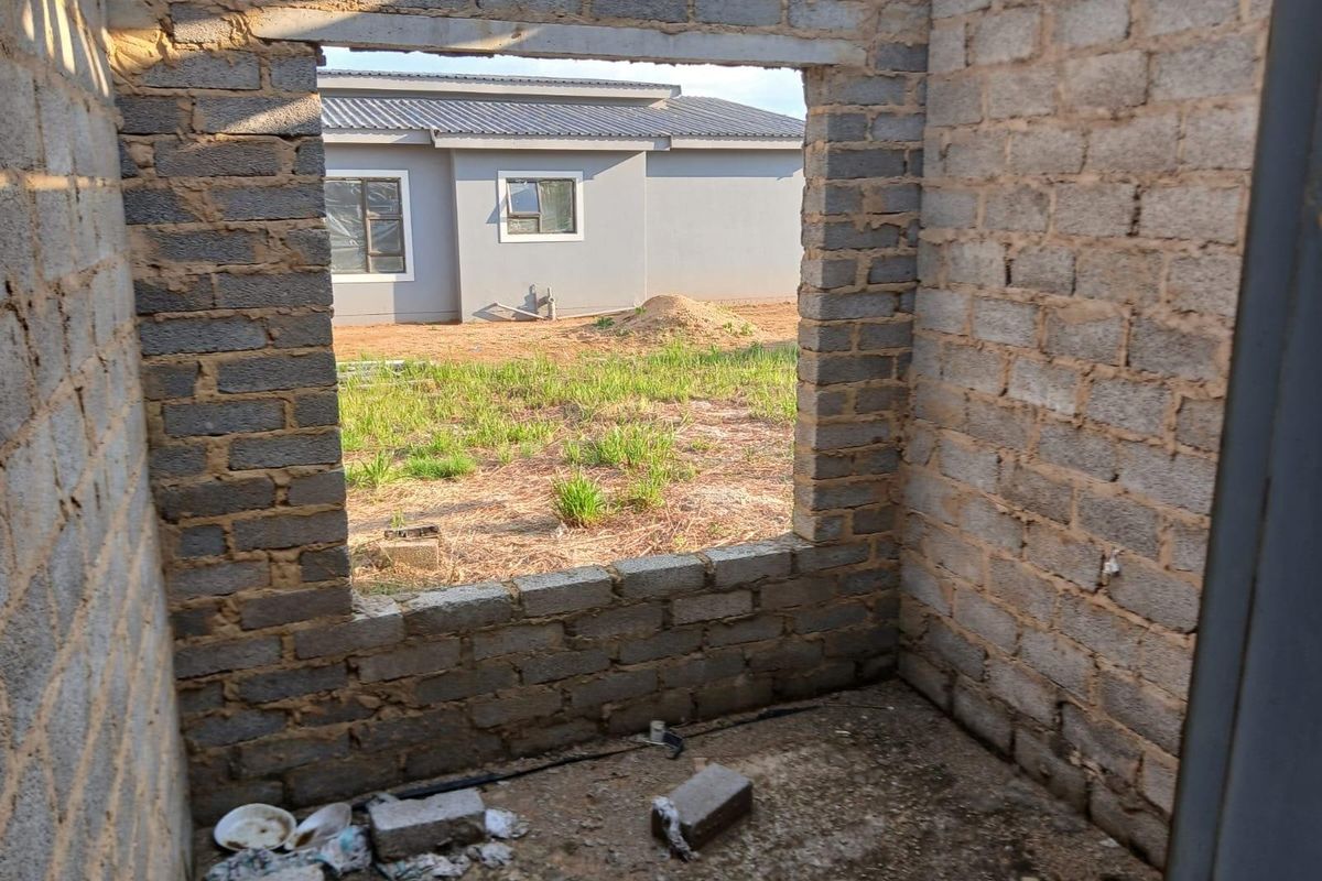 An unfinished bedroom space featuring exposed brick walls and a concrete floor, currently in the construction phase.