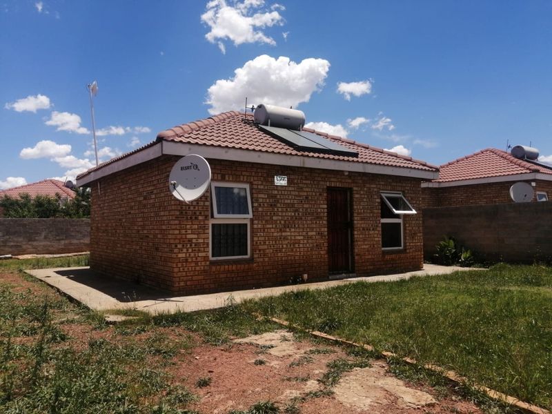 A detached face brick house featuring a tiled roof, solar water heating system, and a surrounding yard with a boundary wall.