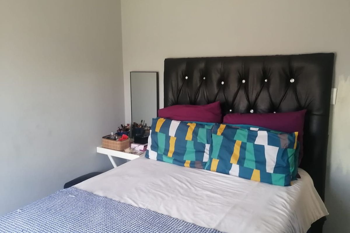 A standard bedroom featuring a tufted headboard and neutral wall finishes, currently showing signs of incomplete painting near the light switch.