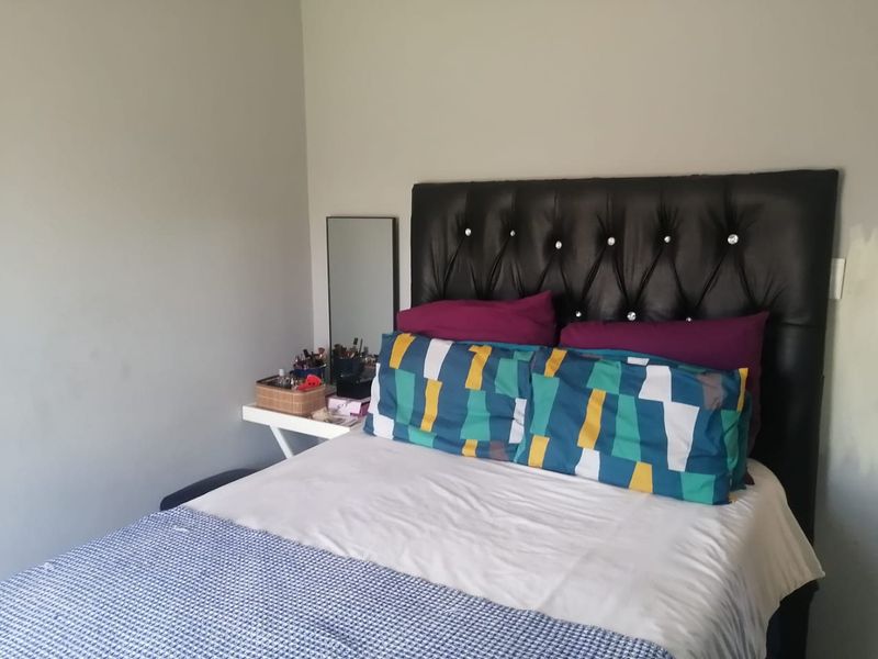 A standard bedroom featuring a tufted headboard and neutral wall finishes, currently showing signs of incomplete painting near the light switch.