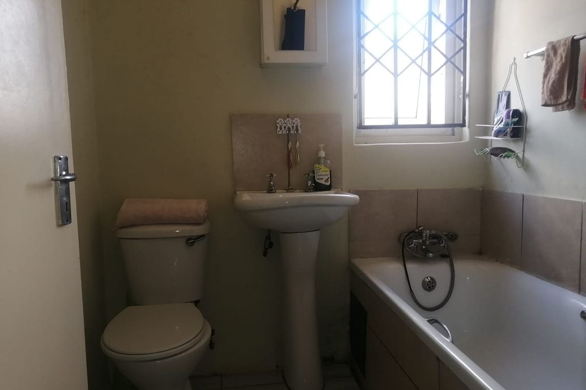 A compact bathroom featuring a pedestal washbasin, standard toilet, and a bathtub with tiled splashbacks and security bars on the window.