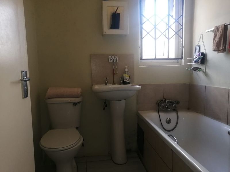 A compact bathroom featuring a pedestal washbasin, standard toilet, and a bathtub with tiled splashbacks and security bars on the window.