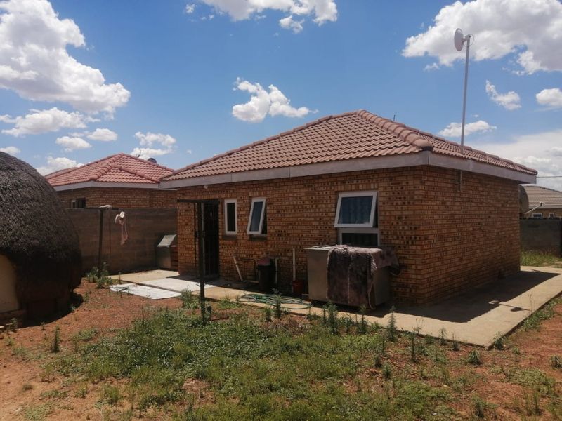 Rear view of a face brick house featuring a tiled roof, casement windows, and a concrete apron leading to the backyard.