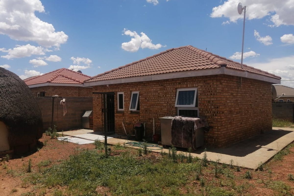 Rear view of a face brick house featuring a tiled roof, casement windows, and a concrete apron leading to the backyard.