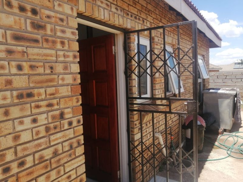 Rear exterior view of the house featuring face brick walls, a timber entrance door, and a security gate.