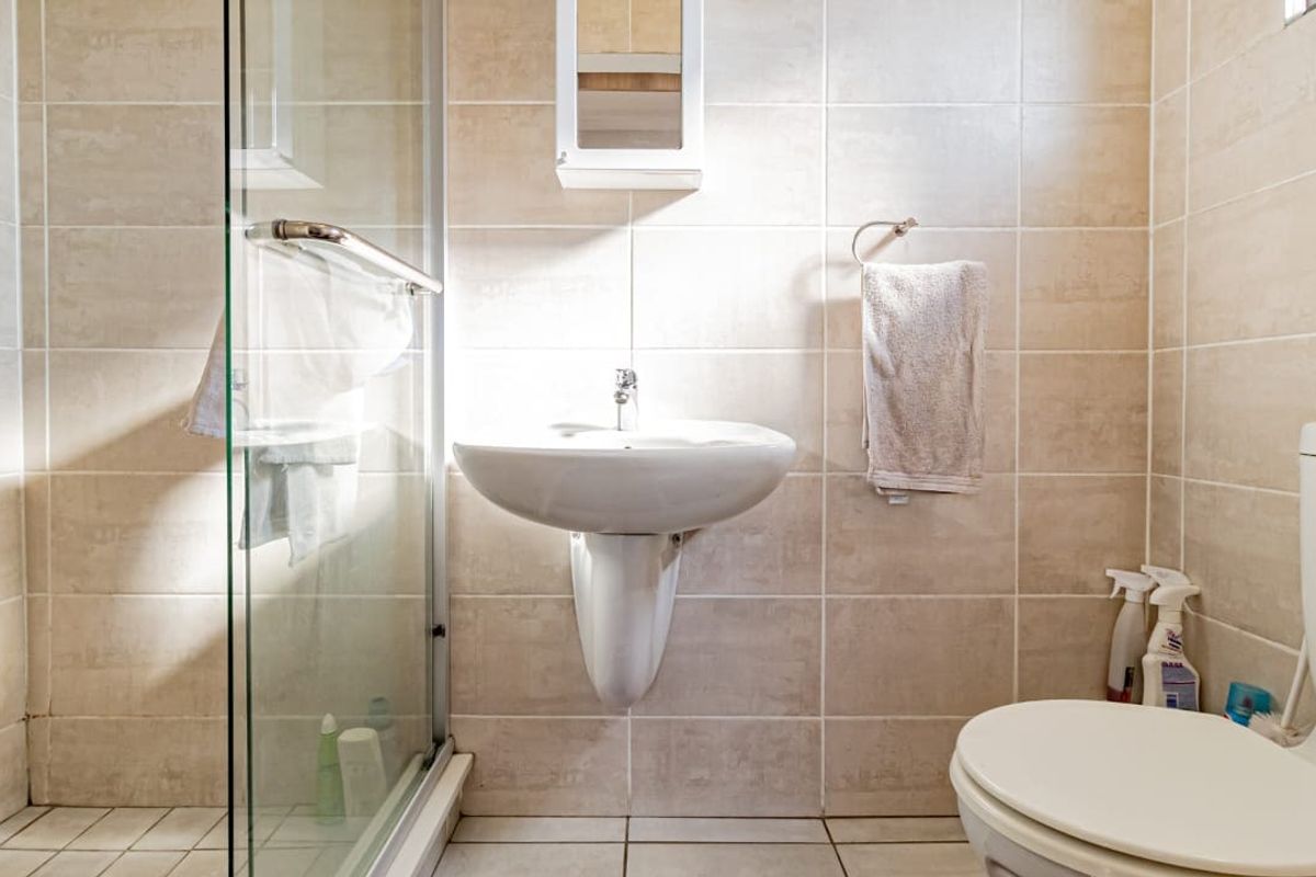 A functional bathroom featuring a glass shower enclosure, pedestal basin, and wall-mounted medicine cabinet with neutral ceramic tiling throughout.