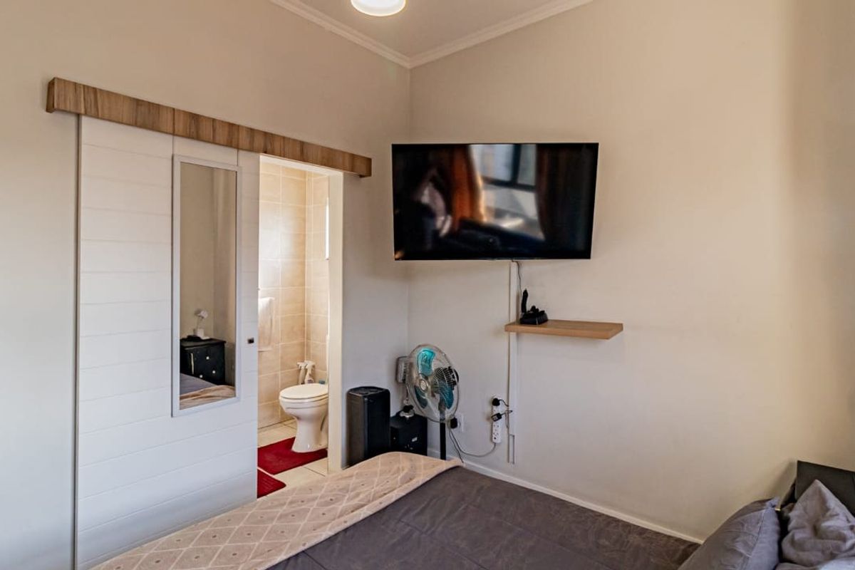 A bedroom featuring a sliding barn door leading to an en-suite bathroom, with a wall-mounted television and floating shelf.