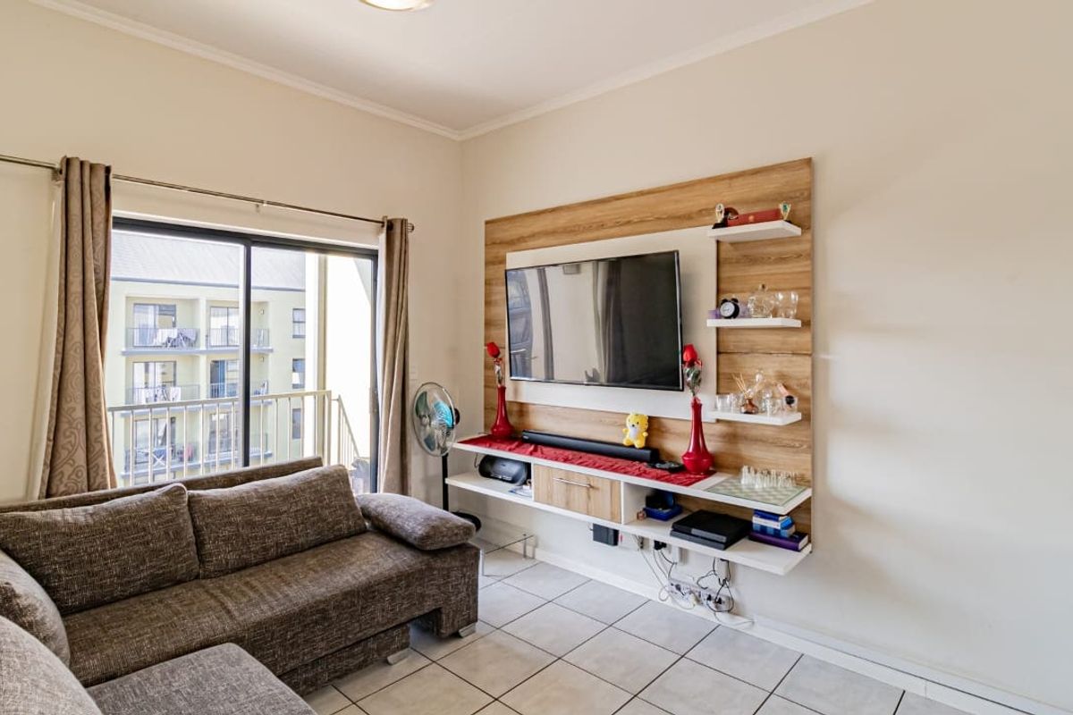 A living room featuring tiled flooring, a built-in media wall unit, and sliding glass doors providing access to a balcony.