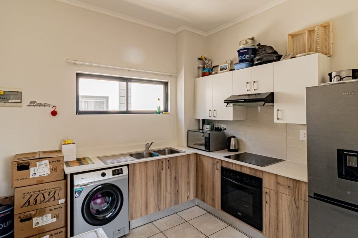 Compact kitchen featuring wood-look cabinetry, integrated oven and hob, stainless steel sink, and tiled flooring with a dedicated space for a washing machine.