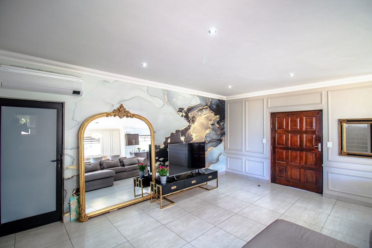 A well-maintained living room featuring decorative wainscoting, tiled flooring, recessed lighting, and a statement feature wall with a modern air conditioning unit.