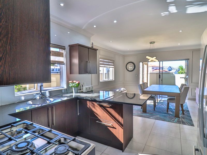 Open-plan kitchen and dining area featuring dark wood cabinetry, granite countertops, gas hob, and sliding doors leading to an outdoor space.