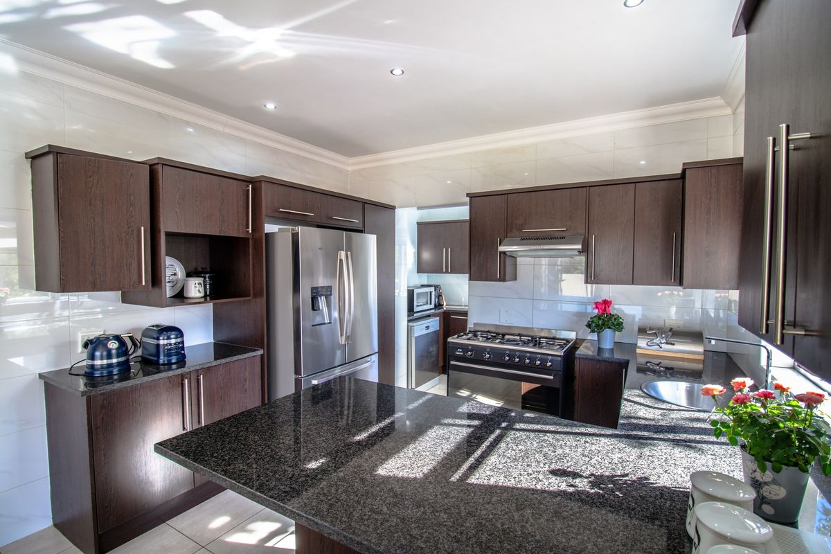 Modern kitchen featuring dark wood cabinetry, granite countertops, a gas stove with extractor fan, and recessed lighting.