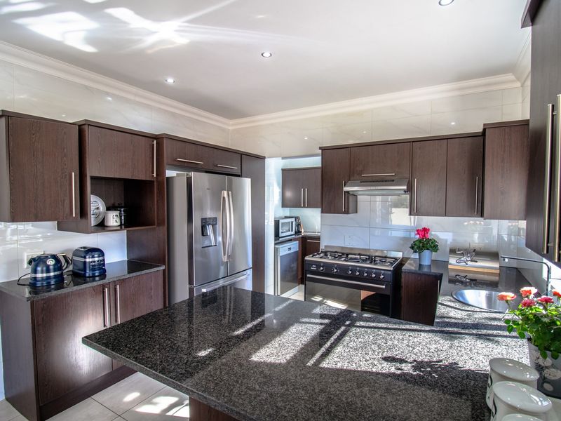 Modern kitchen featuring dark wood cabinetry, granite countertops, a gas stove with extractor fan, and recessed lighting.