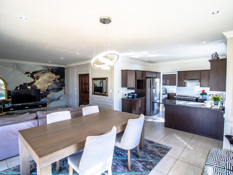 Spacious open-plan living, dining, and kitchen area featuring dark wood cabinetry, stone countertops, modern lighting, and elegant wall paneling.