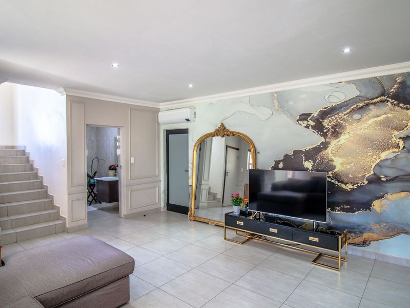 Spacious living room featuring tiled flooring, recessed downlighting, decorative wall molding, and a wall-mounted air conditioning unit, with an adjacent staircase.