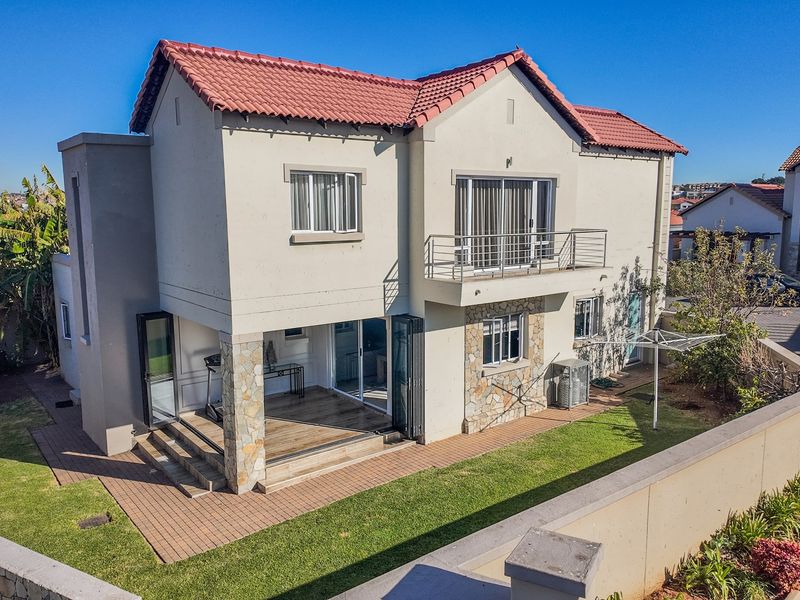 Rear view of a double-story townhouse featuring a tiled roof, stone cladding accents, a balcony with metal railing, and a paved patio area.