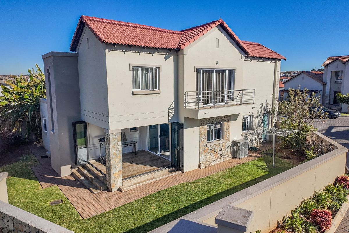 Rear view of a double-story townhouse featuring a tiled roof, stone cladding accents, a balcony with metal railing, and a paved patio area.