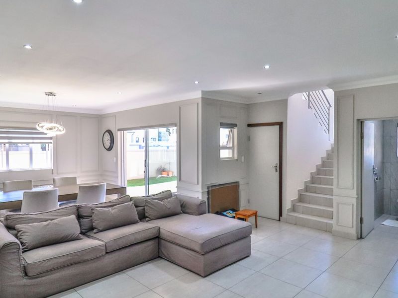 Spacious open-plan living and dining area featuring elegant wainscoting, tiled floors, recessed lighting, and direct access to the rear patio and staircase.