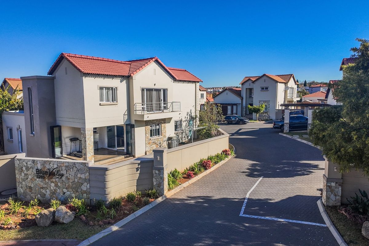 Aerial view of a residential townhouse complex featuring paved driveways, stone-clad exterior walls, and terracotta roof tiles under a clear blue sky.