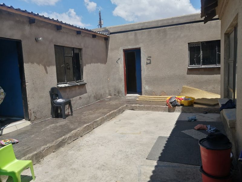 A rear courtyard area featuring a concrete patio and multiple access points to the dwelling, showing signs of significant wear and weathering.
