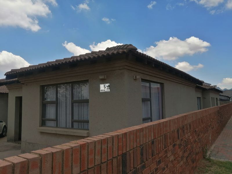 Front exterior view of a single-story house featuring a tiled roof, textured facade, and a brick boundary wall.