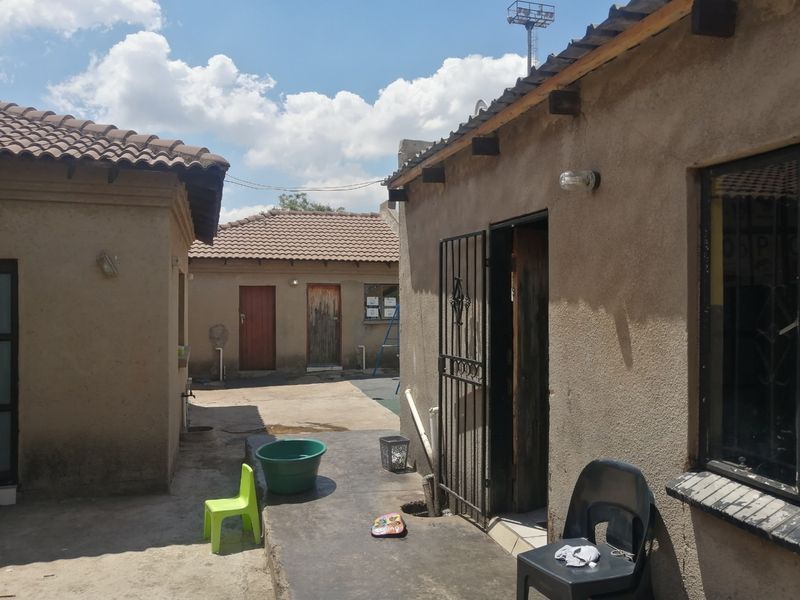 Rear courtyard area featuring concrete paving, multiple building access points, and tiled roof structures.