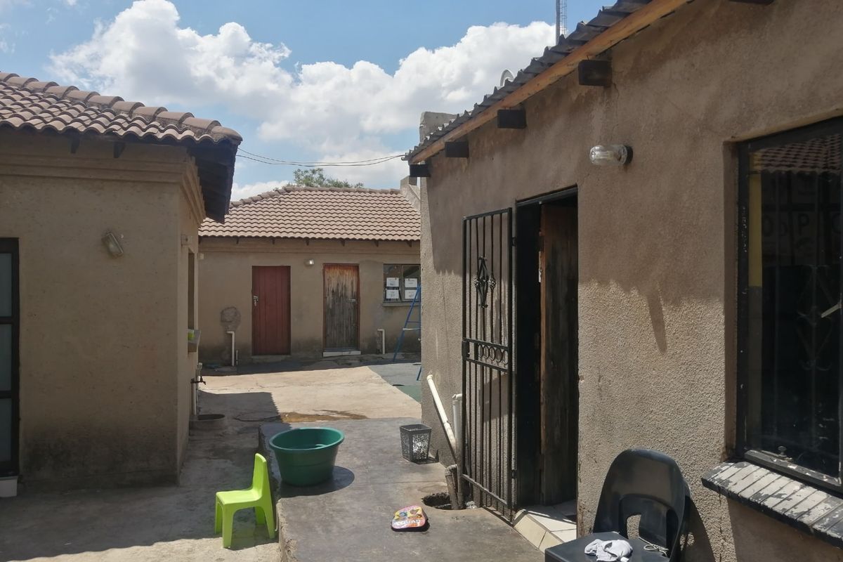 Rear courtyard area featuring concrete paving, multiple building access points, and tiled roof structures.