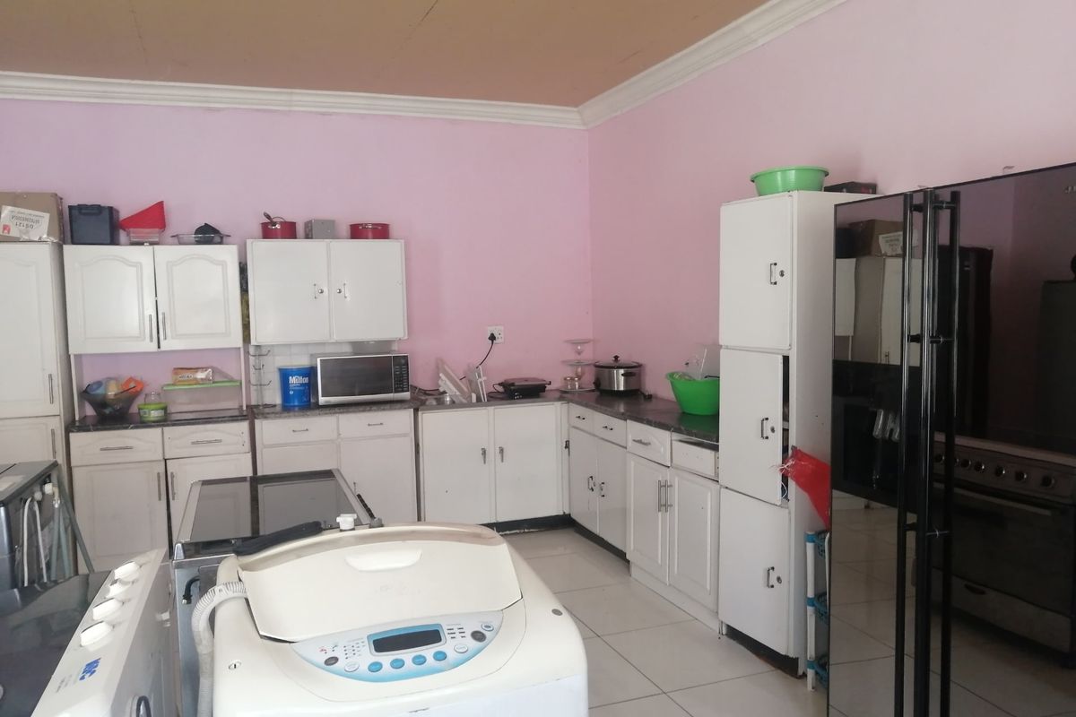 A functional kitchen featuring white built-in cabinetry, laminate countertops, and tiled flooring, offering a practical layout with potential for modern cosmetic updates.